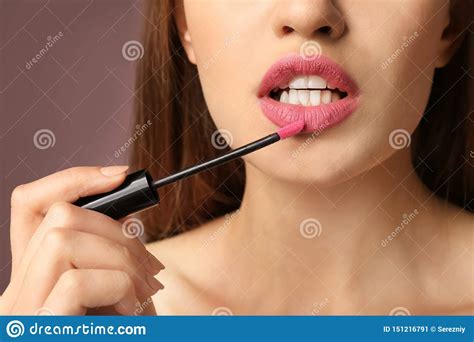 Beautiful Young Woman Applying Pink Lipstick On Color Background
