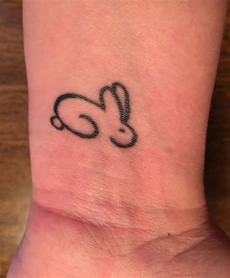 a small tattoo on the wrist of a person with a bunny ear ring in it