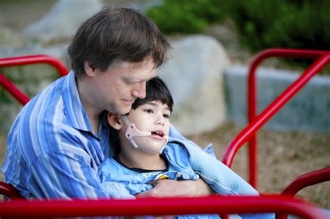 Father Holding Disabled Son On Merry Go Round At Playground Davis