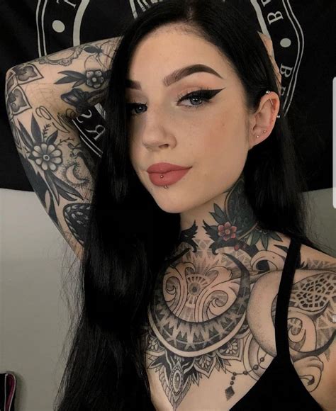 a woman with tattoos on her chest posing for the camera in front of a