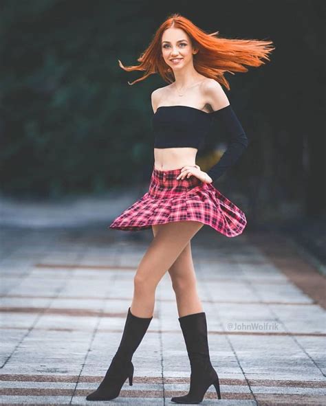 A Woman With Long Red Hair Wearing A Black Top And Pink Plaid Skirt
