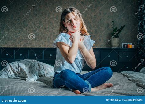 A Young Brunette Girl Sits On A Bed In Her Room She Has A Sore Throat