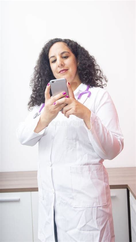 Female Latin Female Doctor Smiling Standing Looking At Her Phone In Her
