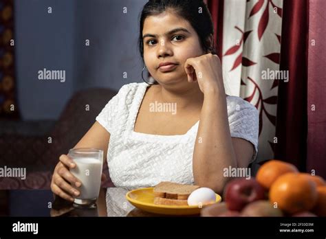 An Indian Asian Woman Holding A Glass Of Milk Sitting Beside A Table In
