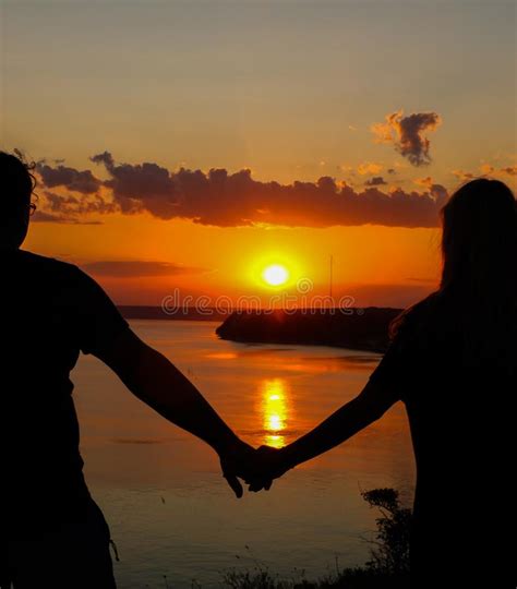 Silhouette Of Romantic Couple Holding Hands On The Beach And Looking At