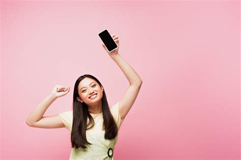 smiling asian girl with clenched fist holding smartphone with blank
