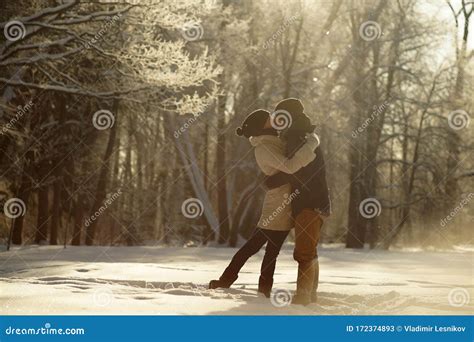 Young Couple Hugging And Kissing In Sunny Snowy Forest Background Of