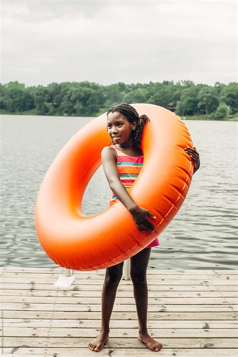 african american girl holding an orange tube by a lake by stocksy