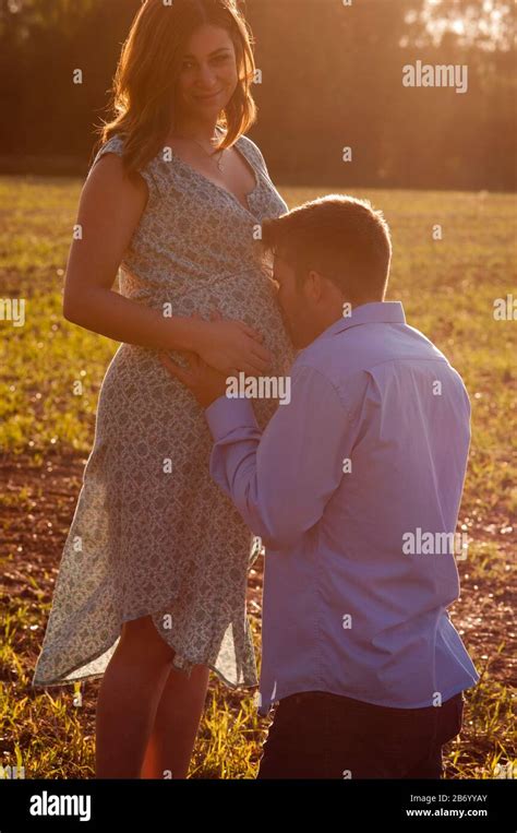 Pregnant Young Woman Standing In A Field With Her Partner Kissing Her