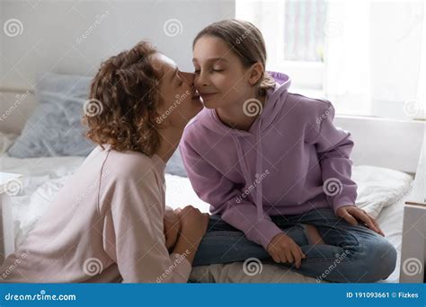 loving mother kissing adorable teenage pretty daughter on cheek stock