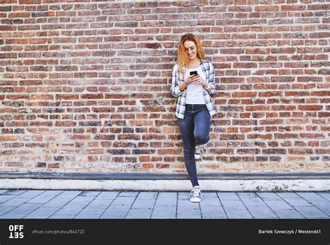 young woman leaning  brick wall   city   smartphone stock photo offset