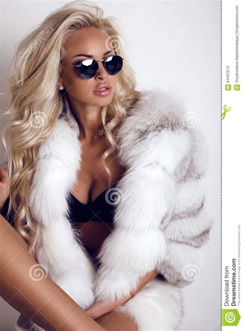woman with long blond hair wears luxurios fur coat and sunglasses stock