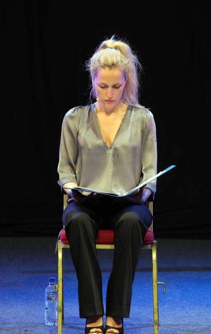 gillian anderson sitting on a chair while reading