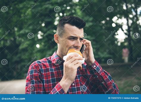 Handsome Young Man Eating Sandwich Autdoor He Is Holding A Phone Stock