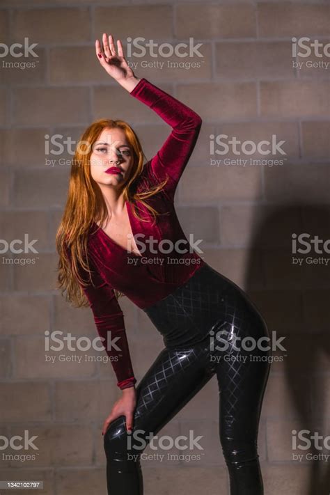 redhaired girl in latex brown and black tight suit on a brick wall