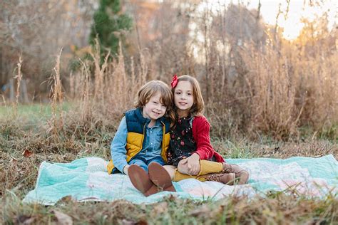 cute brother and sister sitting together on a blanket by stocksy