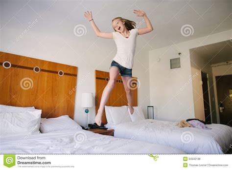 a blond teen girl jumping on beds in a hotel royalty free