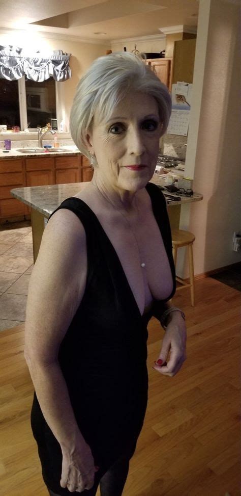 an older woman with white hair is standing in a kitchen and posing for