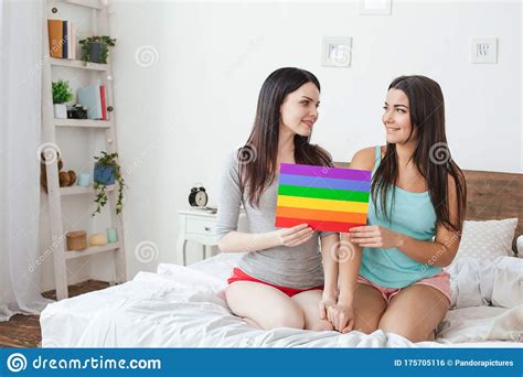 lesbian couple in bedroom at home sitting holding lgbt