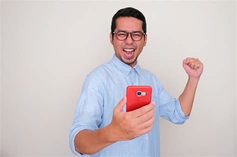 adult asian man clenched fist showing excitement while holding a mobile