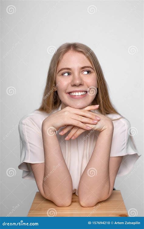 Young Smiling Blonde Girl Puts Her Head On Hands Rests On Stool
