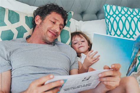 dad and daughter bonding while reading in bed together by stocksy
