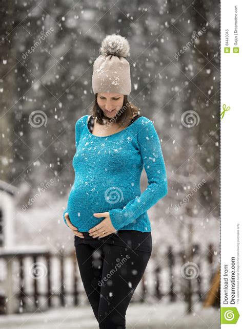 happy pregnant woman standing outside in snowfall stock