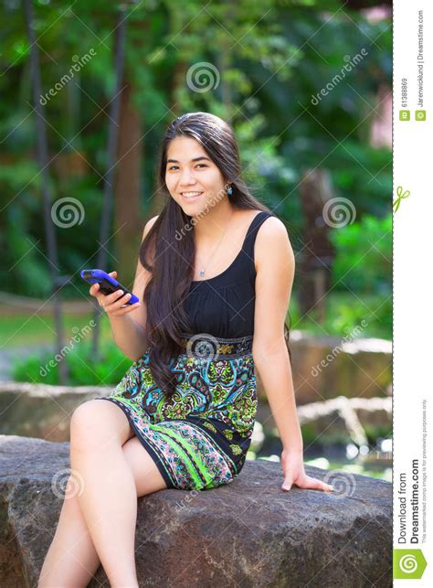 biracial teen girl sitting on rock looking at cellphone stock image image of stone technology