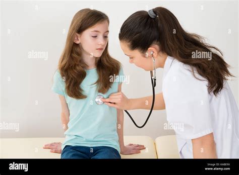 Young Female Doctor Examining Girl With Stethoscope In Hospital Stock