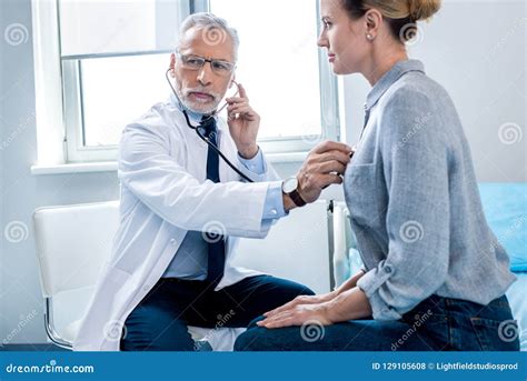Concentrated Mature Male Doctor Examining Female Patient By Stethoscope