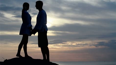 silhouettes of two lovers seated on the beach sunrise sunset stock