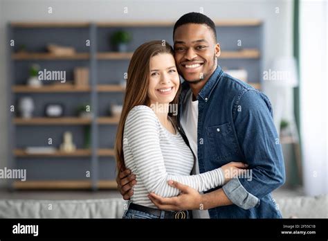 Portrait Of Romantic Interracial Couple Embracing And Smiling At Camera
