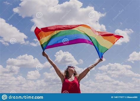 woman holding the gay rainbow flag over blue and cloudy sky outdoors