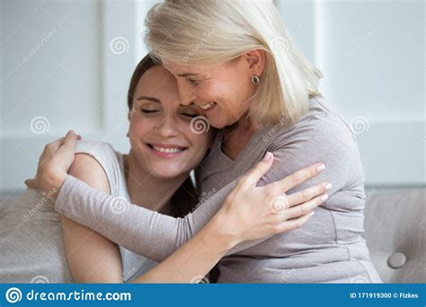 Happy Mature Mom Hug Grownup Daughter Relaxing At Home Together Stock
