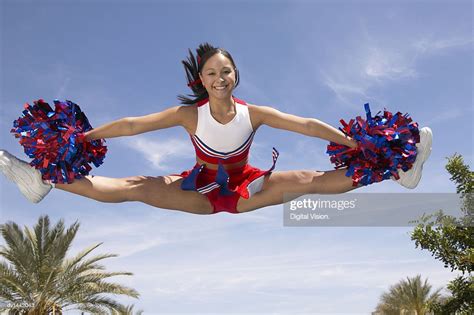 portrait of a cheerleader holding pompoms doing the splits midair photo
