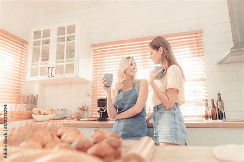 Happy Lesbian Couple Holding Cups Of Coffee In Kitchen Couple Of