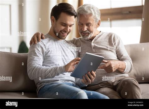 Grownup Son Teaching Elderly Mature Father Using Applications On Tablet