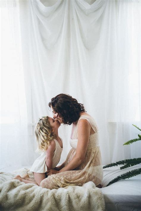 a mother kissing her daughter on the cheek while sitting on a bed in