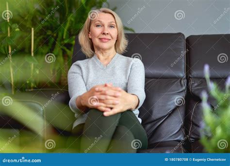 Lovely Middle Aged Blond Woman Sitting On A Sofa At Home Looking At The