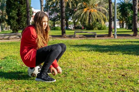Preteen Girl Sitting On Top Of Her Soccer Ball In The Park On A Sunny