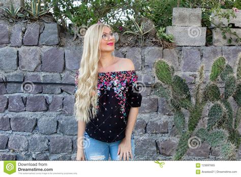 beautiful blonde woman in glasses standing near a stone