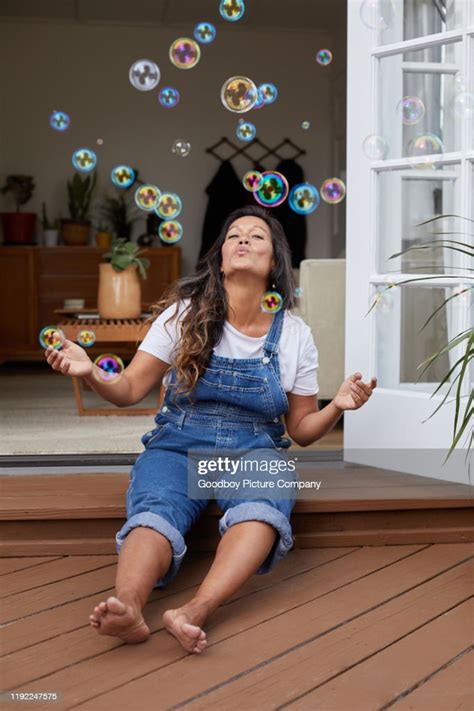 Smiling Mature Woman Sitting On Her Patio Blowing Bubbles High Res