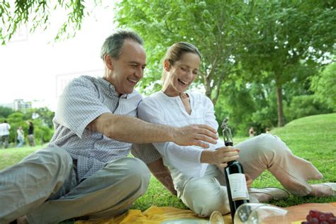 Mature Couple Having Picnic Outdoors Opening Bottle Of Wine Stock