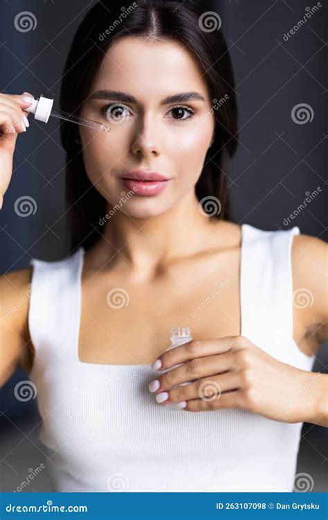 Cheerful Woman Standing In Front Of Mirror At Home Using Serum For