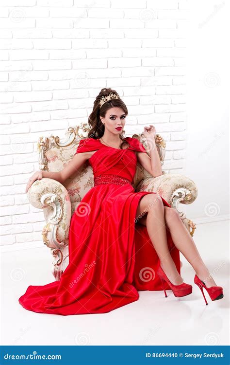 Elegant Woman In A Long Red Dress Sitting On A Vintage Chair In Stock