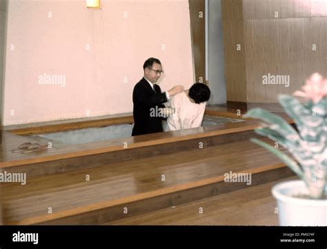 Priest Baptizing A Japanese Woman Who Bows Her Head In A Christian