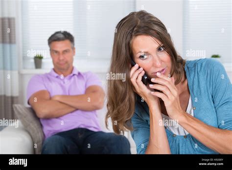 Mature Woman Talking Secretly On Mobile Phone In Front Of Her Husband