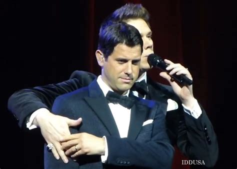 Two Men In Tuxedos Are Performing On Stage With Microphones To Their Ears