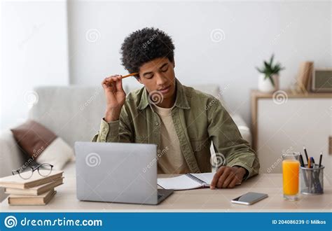 thoughtful black teen guy passing hard exam or online test on laptop at