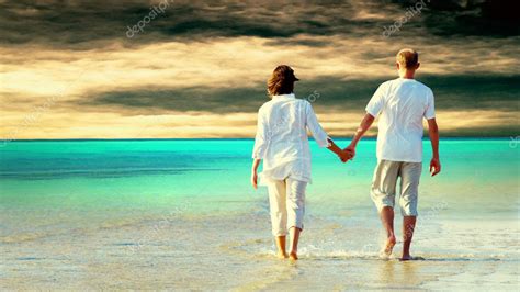 Rear View Of A Couple Walking On The Beach Holding Hands